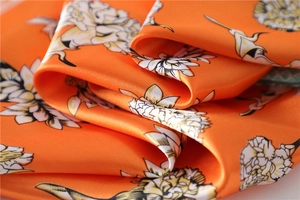Macro shot of orange floral silk scarf fabric with elegant satin texture and smooth drape
