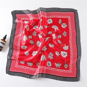 Macro detail of red satin silk scarf featuring white floral patterns and checkered border