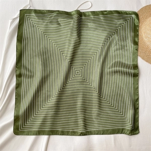 Flat lay of a dark green silk scarf with geometric square patterns on white silk backdrop