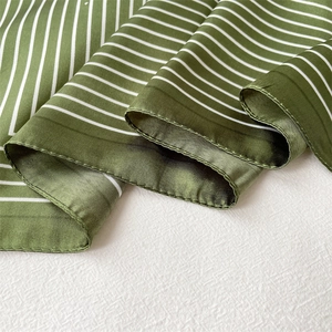 Detailed view of striped green and white silk scarf with smooth satin texture and rolled hem