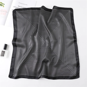 Detail of a square silk scarf with black and white geometric stripes on a white surface