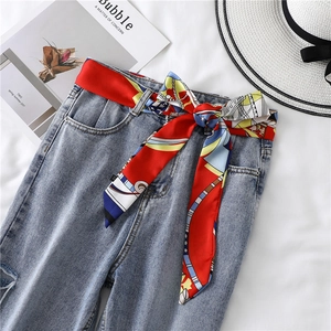 Detail of light blue washed denim jeans with a red floral silk scarf belt tied in a bow