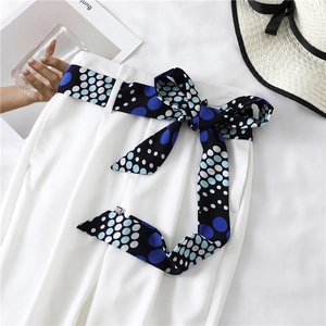 Detail of navy blue polka dot scarf belt tied on white linen summer trousers