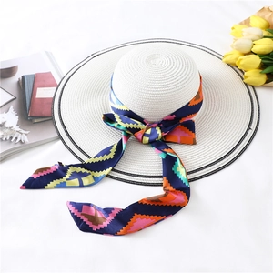 Detail of white straw sun hat featuring a colorful geometric silk scarf and black striped edge