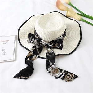 Detail of white straw sun hat with elegant black baroque print ribbon and long bow