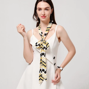 Close-up of a long narrow silk scarf with black and yellow polka dots on cream white