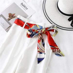 Close-up of a colorful baroque print silk scarf tied as a belt on white wide-leg trousers