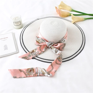 Detail of pink satin ribbon with gold chain patterns tied on a white woven sun hat