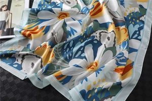 Detailed view of floral satin silk scarf featuring white daisies and yellow flowers on blue