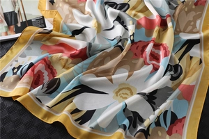 Detail of elegant floral silk scarf with yellow border draped on a textured surface