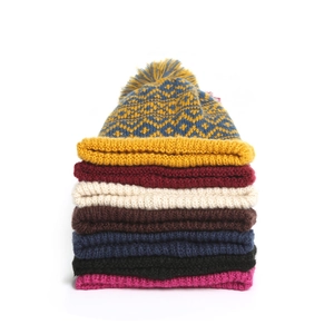 Stack of colorful knitted beanies with faux fur pom poms showing winter color options