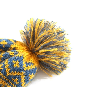 Detail of blue and yellow knitted hat with a large two-tone pom-pom and geometric patterns