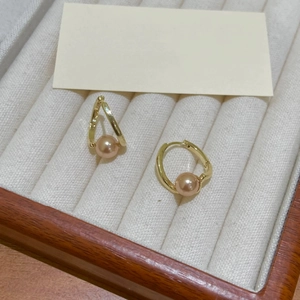 Élégantes créoles dorées avec perles roses rondes sur un plateau à bijoux en velours blanc