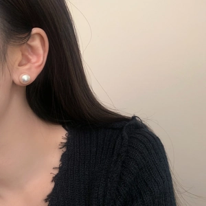 Close-up of elegant round white pearl earring with iridescent luster worn by model