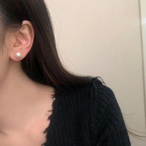 Close-up of a white pearl earring worn on the earlobe with a black knit sweater background