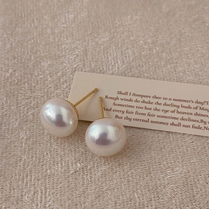 Detail of round pearl earrings with iridescent luster on a warm textured fabric background