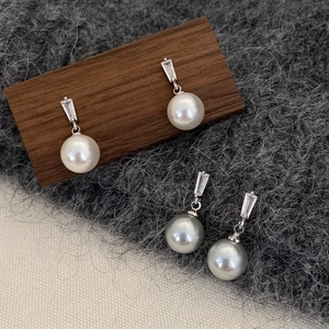 Close-up of pearl drop earrings with rectangular zircon studs in white and grey colors