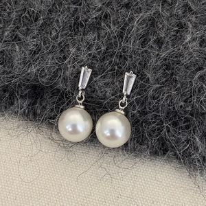 Close-up of elegant pearl earrings with rectangular zircon on textured fabric