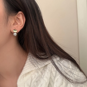 Detail of elegant gold geometric earring with grey pearl drop on a model's ear