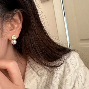 Close-up of elegant gold circular stud earrings with hanging white round pearls on model