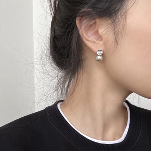 Close-up of minimalist silver disc and grey pearl drop earrings worn by a female model