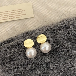 Detailed view of large white pearl earrings with hammered gold metal texture on wool fabric