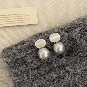 Detail of silver geometric pearl earrings on a textured wool fabric background