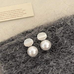 Detailed close-up of pearl pendant earrings with silver oval metal on a textured background