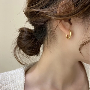 Close-up of minimalist 18k gold-plated hoop earring worn by a model in soft lighting