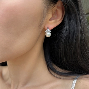 Close-up of crown-shaped pearl earring with sparkling zircons worn by a model