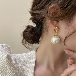 Detailed shot of a large baroque pearl earring with matte gold ring on a female model