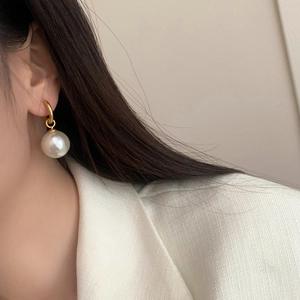 Close-up of a large white pearl drop earring with a matte gold hoop on a female model