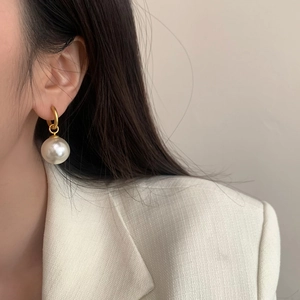 Close-up of elegant gold pearl drop earring worn by a model in a white textured suit