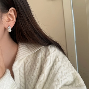 Close-up of pearl stud earring with a sparkling crown setting worn by a model