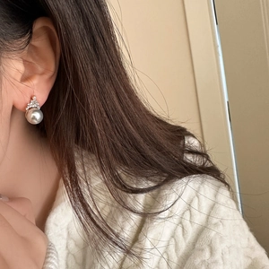 Close-up of crown-shaped zirconia earrings with a grey pearl on a model's ear