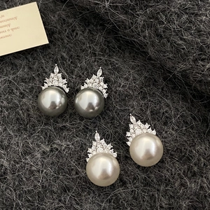 Detail of elegant pearl earrings with crown-shaped zircon settings on gray knit fabric