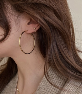 Nahaufnahme eleganter goldener Creolen und minimalistischer Kugelstecker an einem Model