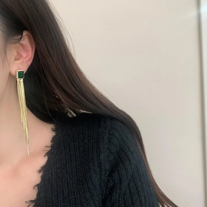 Detailed view of long tassel earrings with green rectangle stone and gold metal chains