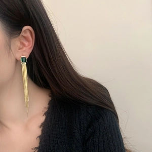 Elegant gold tassel earrings with green emerald-cut gemstone on a female model