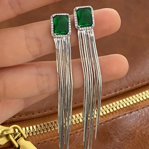 Close-up of emerald green tassel earrings with silver chains and crystal rectangle stud