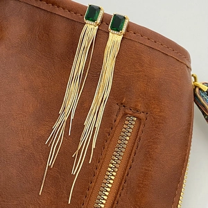 Detail of long gold tassel earrings with a rectangular green gemstone and pavé accents