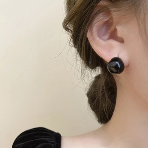 Detail of elegant black pebble-shaped stud earrings with glossy finish on a female model
