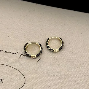 Detail of gold twisted hoop earrings with black enamel spiral texture and polished finish