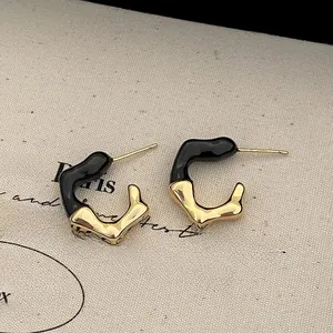 Macro shot of French style irregular gold-plated earrings with black drip glaze detail