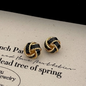 Macro shot of French style gold-plated knot earrings with black enamel textured inlay