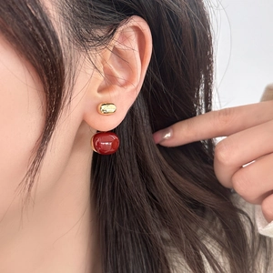 Retro gold oval stud earrings with round red glazed pendants worn by a female model
