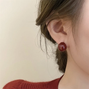 Close-up of elegant deep burgundy spherical stud earrings worn by a model in soft light