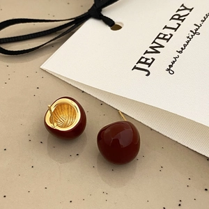 Close-up of deep red glazed ball earrings with elegant gold metal base and needle