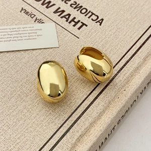 Macro detail of gold oval eggshell earrings resting on a vintage book surface