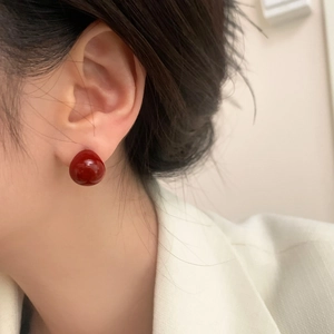 Classic burgundy spherical stud earrings with glossy finish on elegant female model